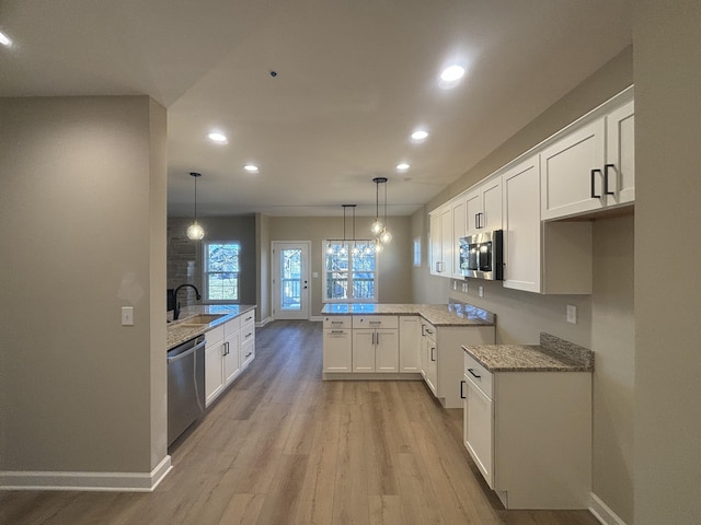 kitchen with decorative light fixtures, light wood-type flooring, appliances with stainless steel finishes, kitchen peninsula, and white cabinets