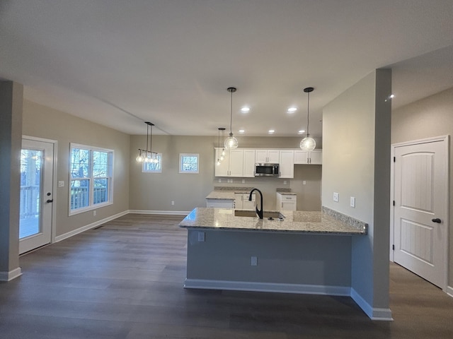 kitchen with hanging light fixtures, light stone counters, white cabinets, dark hardwood / wood-style flooring, and kitchen peninsula