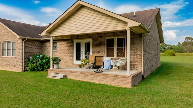 rear view of property featuring french doors, a patio, and a lawn