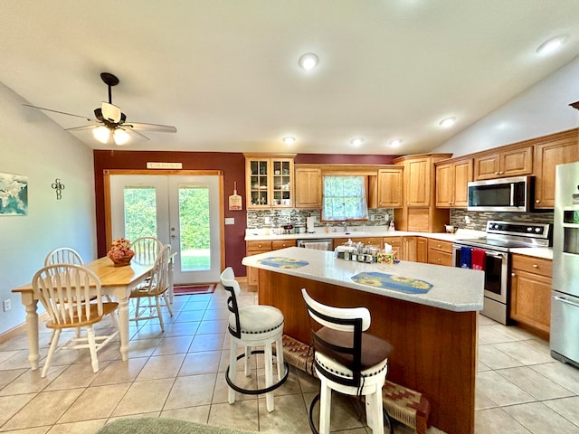 kitchen featuring appliances with stainless steel finishes, light tile patterned flooring, vaulted ceiling, and a center island