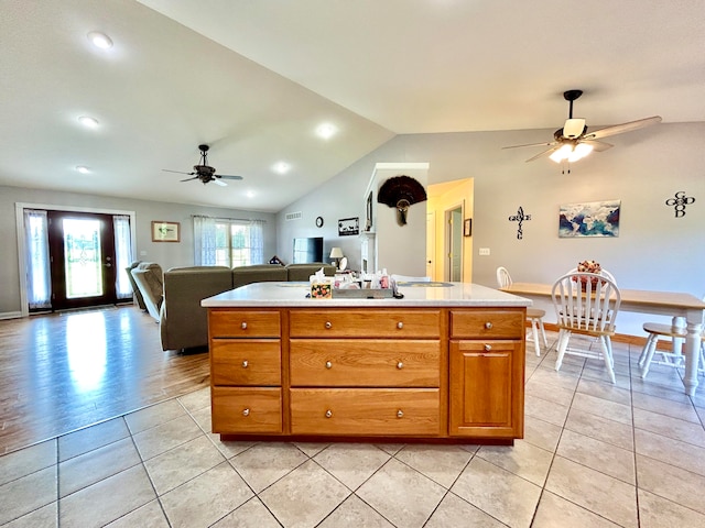 kitchen with an island with sink, light tile patterned floors, ceiling fan, and vaulted ceiling