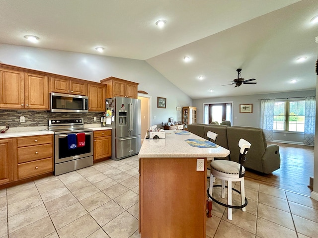 kitchen with a breakfast bar area, stainless steel appliances, decorative backsplash, a center island, and light tile patterned floors