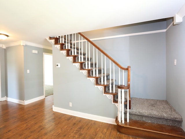 staircase with wood-type flooring and ornamental molding