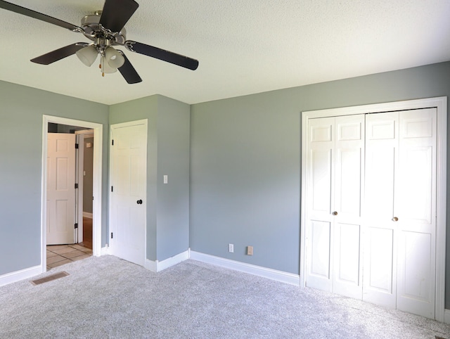 unfurnished bedroom with ceiling fan, light carpet, a closet, and a textured ceiling