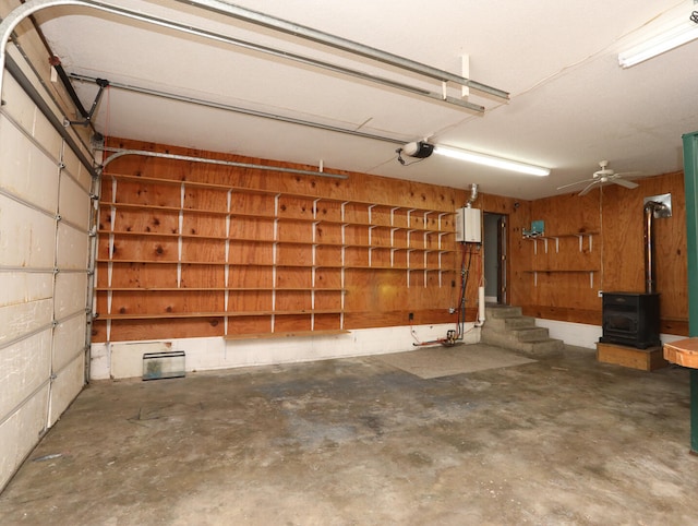 garage featuring ceiling fan, wooden walls, a garage door opener, and a wood stove