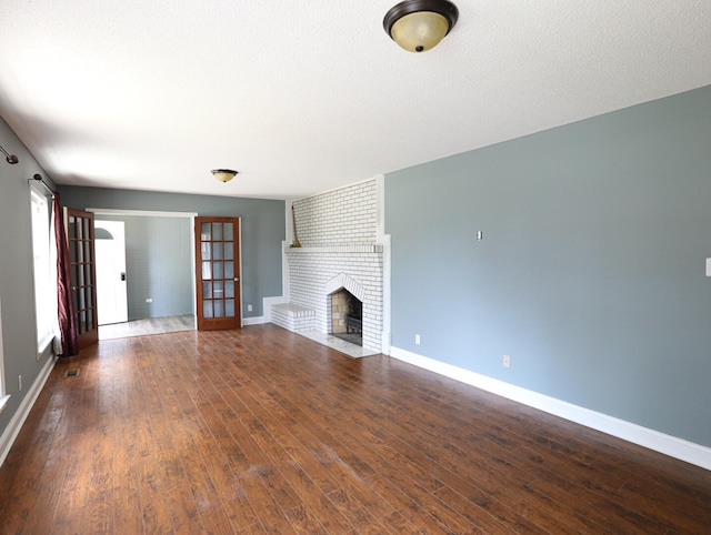 unfurnished living room with a textured ceiling, brick wall, hardwood / wood-style floors, and a brick fireplace