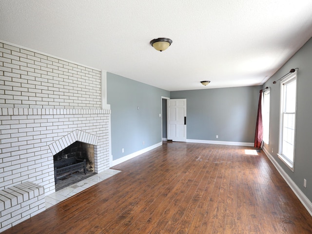 unfurnished living room with a textured ceiling, wood-type flooring, and a brick fireplace