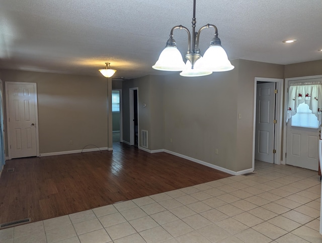 empty room with light wood-type flooring, a wealth of natural light, a notable chandelier, and a textured ceiling