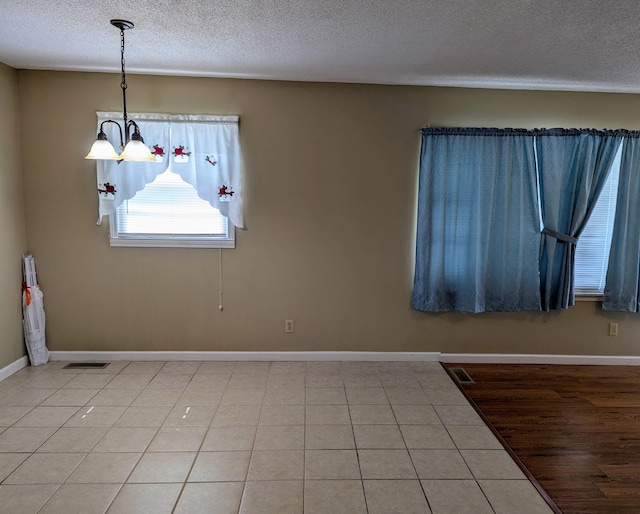 unfurnished dining area with hardwood / wood-style floors, a textured ceiling, and an inviting chandelier