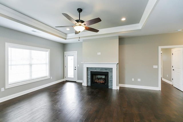 unfurnished living room with ceiling fan, a tray ceiling, dark hardwood / wood-style floors, and a stone fireplace