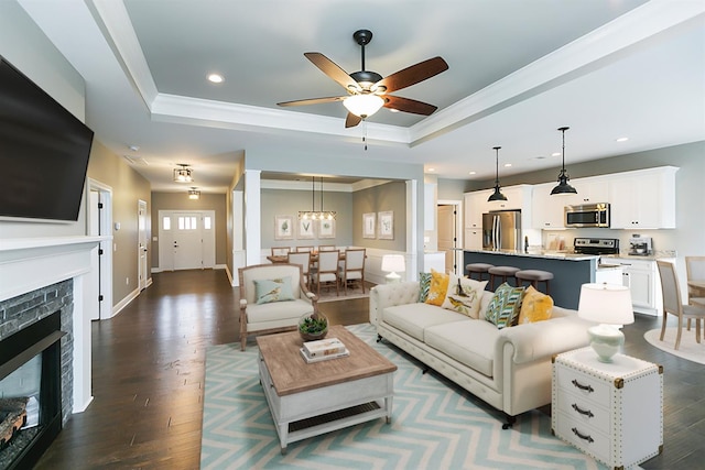 living room featuring ceiling fan with notable chandelier, a raised ceiling, and dark wood-type flooring