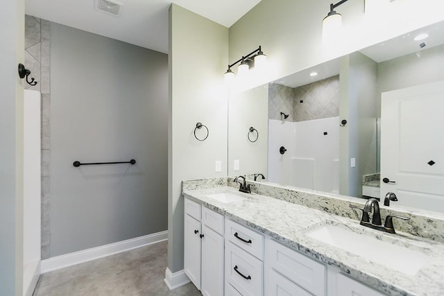 bathroom featuring tile patterned floors, tiled shower, and dual vanity