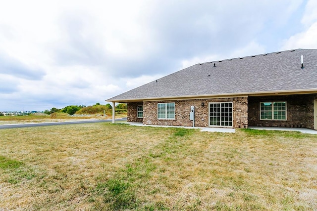 back of property featuring a lawn, a shingled roof, and brick siding