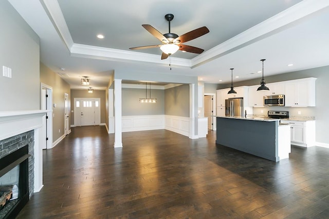 unfurnished living room with a tray ceiling, dark wood-type flooring, ceiling fan with notable chandelier, and ornamental molding