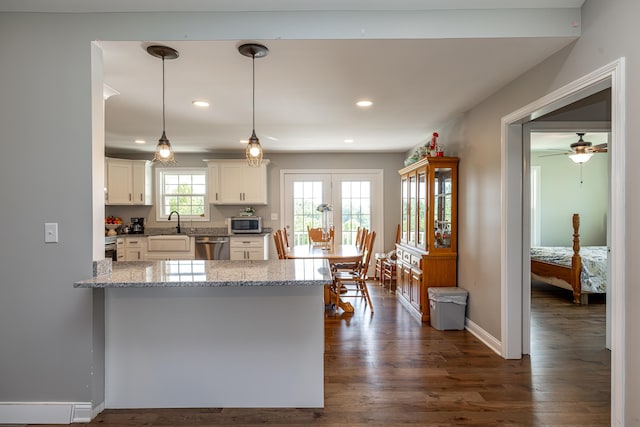 kitchen featuring white cabinets, dark wood-style floors, appliances with stainless steel finishes, a peninsula, and pendant lighting