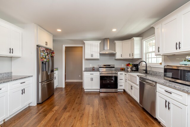 kitchen featuring dark wood-type flooring, light stone countertops, stainless steel appliances, wall chimney range hood, and white cabinets