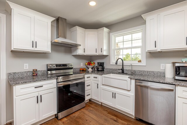 kitchen featuring appliances with stainless steel finishes, dark wood-type flooring, wall chimney range hood, and white cabinets