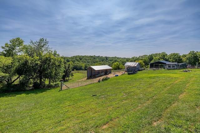 view of yard with a forest view, a pole building, fence, an outdoor structure, and a carport