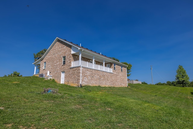 view of side of home with brick siding, a lawn, a balcony, and central air condition unit