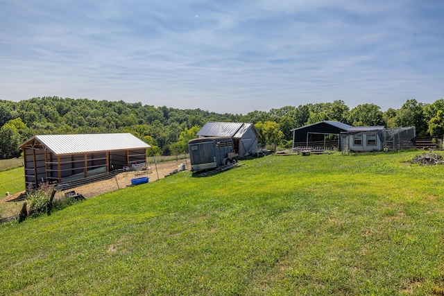 view of yard featuring a carport, an outbuilding, a pole building, and a view of trees