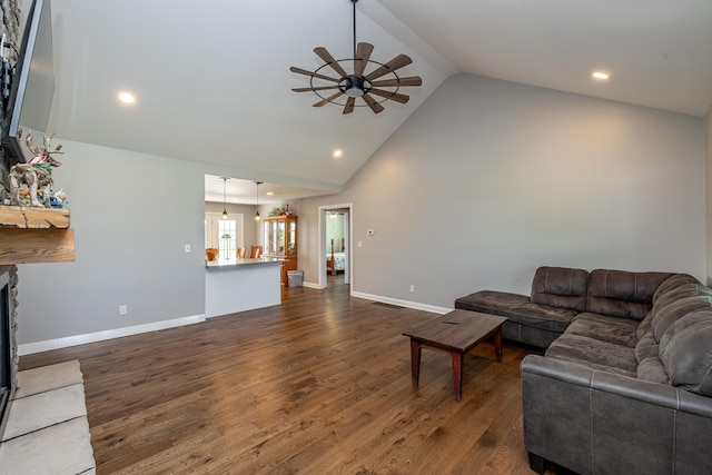 living area with baseboards, a ceiling fan, dark wood-style flooring, a stone fireplace, and high vaulted ceiling