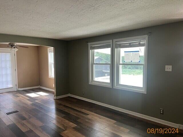 spare room with a textured ceiling, ceiling fan, a healthy amount of sunlight, and dark hardwood / wood-style floors