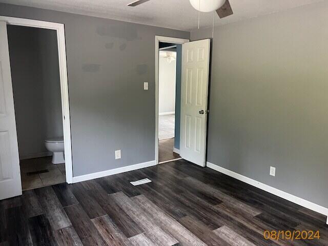 unfurnished bedroom featuring ceiling fan, ensuite bathroom, and dark wood-type flooring