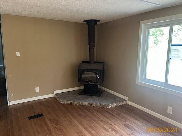 unfurnished living room with a textured ceiling, hardwood / wood-style floors, and a wood stove