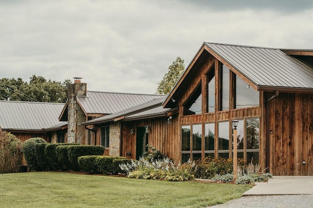 exterior space with metal roof, a yard, a chimney, and stone siding