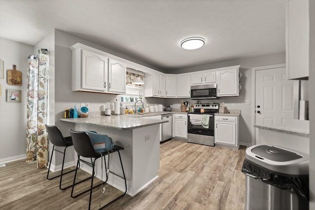 kitchen with light hardwood / wood-style flooring, white cabinetry, light stone countertops, kitchen peninsula, and stainless steel appliances