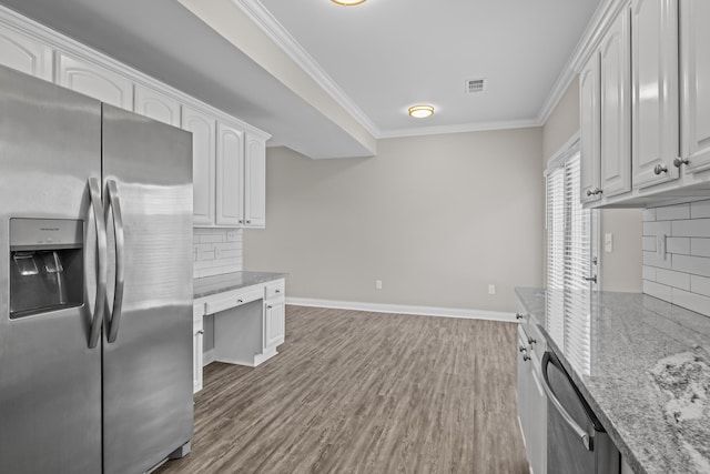 kitchen with stainless steel appliances, white cabinets, crown molding, and light stone countertops