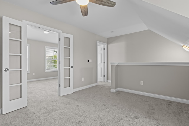 carpeted spare room featuring lofted ceiling, baseboards, a ceiling fan, and french doors