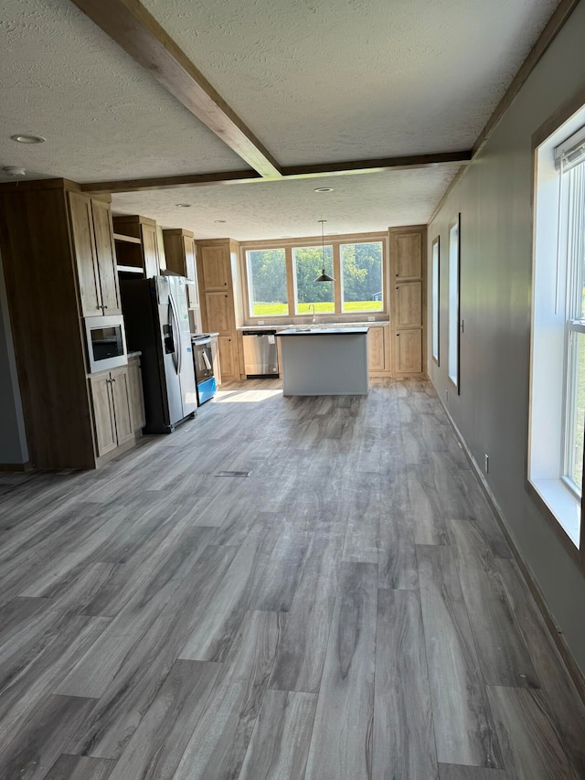 unfurnished living room with beamed ceiling, a textured ceiling, light hardwood / wood-style flooring, and plenty of natural light