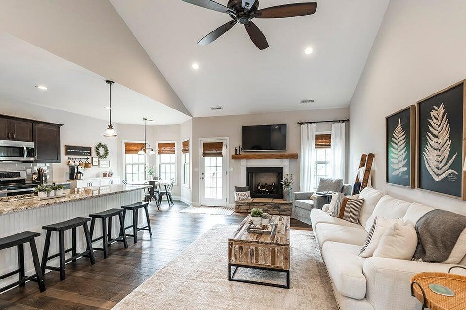 living room with a stone fireplace, dark hardwood / wood-style flooring, ceiling fan, and plenty of natural light