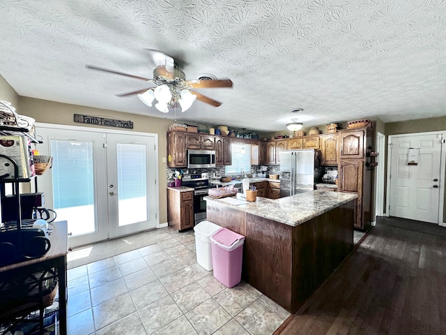 kitchen with a center island, light hardwood / wood-style flooring, stainless steel appliances, ceiling fan, and tasteful backsplash