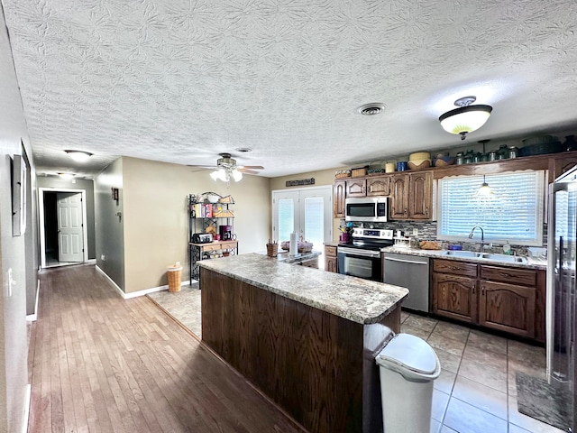 kitchen with a kitchen island, light hardwood / wood-style floors, stainless steel appliances, sink, and ceiling fan