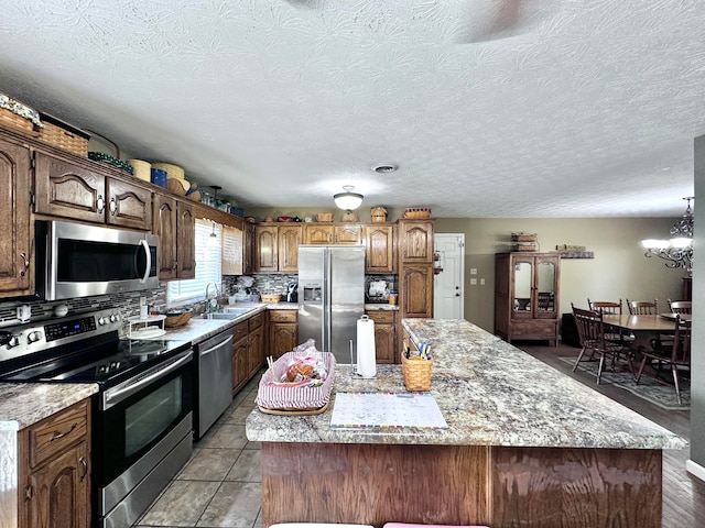 kitchen featuring appliances with stainless steel finishes, an inviting chandelier, a kitchen island, and sink