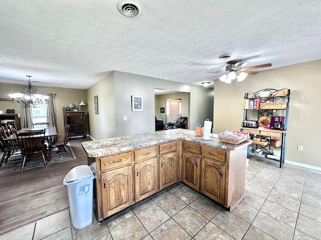 kitchen with hanging light fixtures, light wood-type flooring, ceiling fan with notable chandelier, light stone countertops, and a textured ceiling