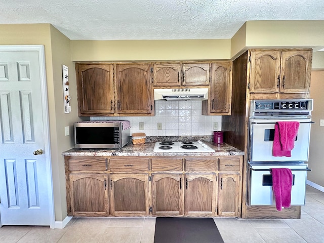 kitchen with white appliances, light tile patterned floors, backsplash, and a textured ceiling