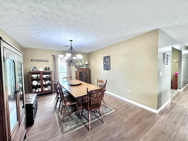 dining area featuring a textured ceiling, wood-type flooring, and an inviting chandelier