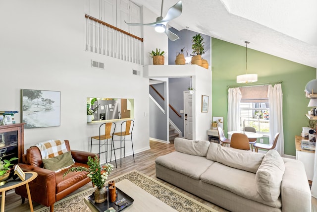 living room featuring ceiling fan, high vaulted ceiling, a textured ceiling, and light hardwood / wood-style flooring