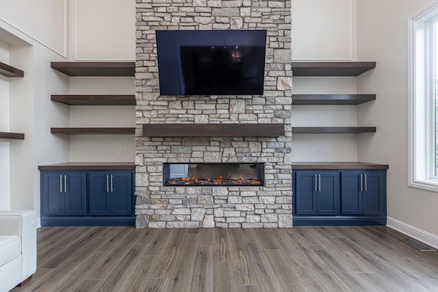 unfurnished living room featuring baseboards, visible vents, dark wood-type flooring, and a stone fireplace