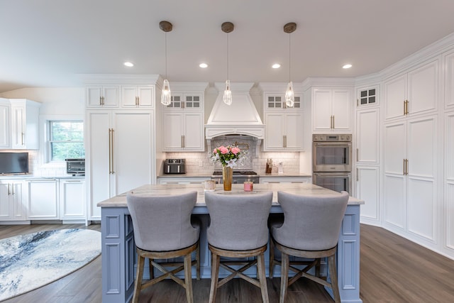 kitchen featuring glass insert cabinets, a kitchen island with sink, premium range hood, and hanging light fixtures