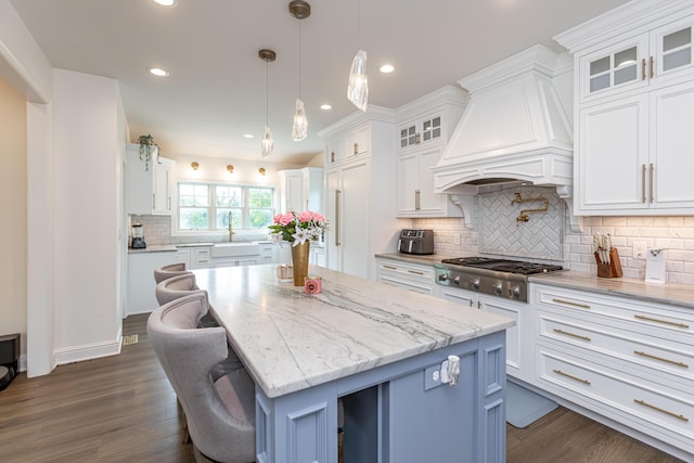 kitchen with glass insert cabinets, a center island, custom exhaust hood, white cabinetry, and stainless steel gas cooktop