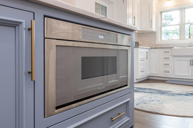 interior details featuring tasteful backsplash, white cabinets, wood finished floors, light countertops, and a sink