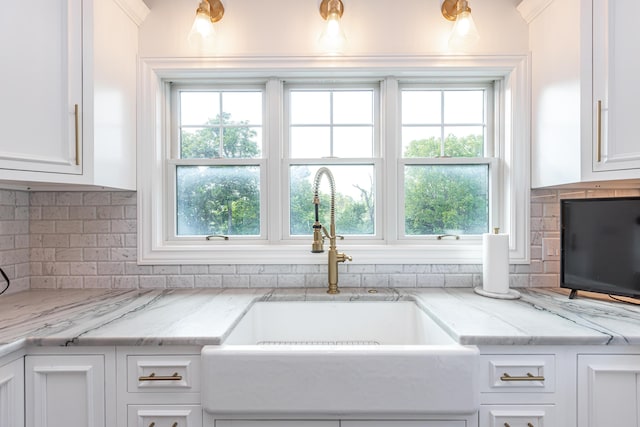 kitchen with light stone counters, a healthy amount of sunlight, white cabinetry, and a sink