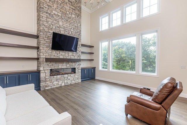 living area featuring light wood-style flooring, a fireplace, a towering ceiling, baseboards, and ornamental molding