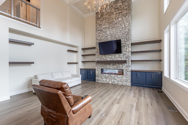 living room featuring a towering ceiling, light wood finished floors, visible vents, and a stone fireplace