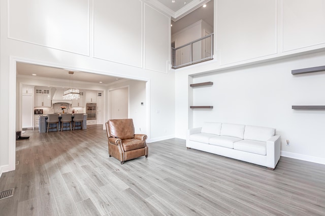 living area with light wood-type flooring, a towering ceiling, baseboards, and crown molding