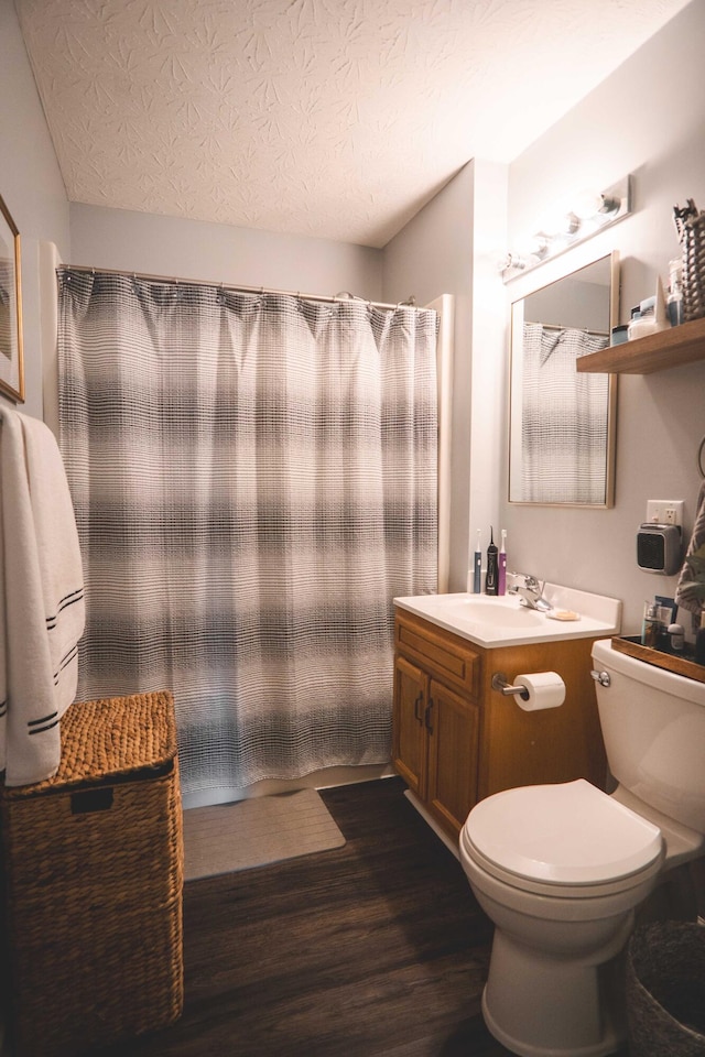 bathroom with wood-type flooring, a textured ceiling, curtained shower, vanity, and toilet